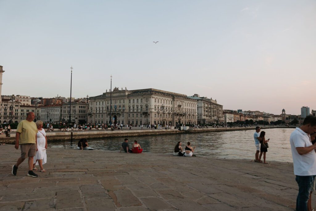 People relaxing along the waterfront in Trieste, Italy with historic buildings and soft evening light creating a calm Mediterranean atmosphere