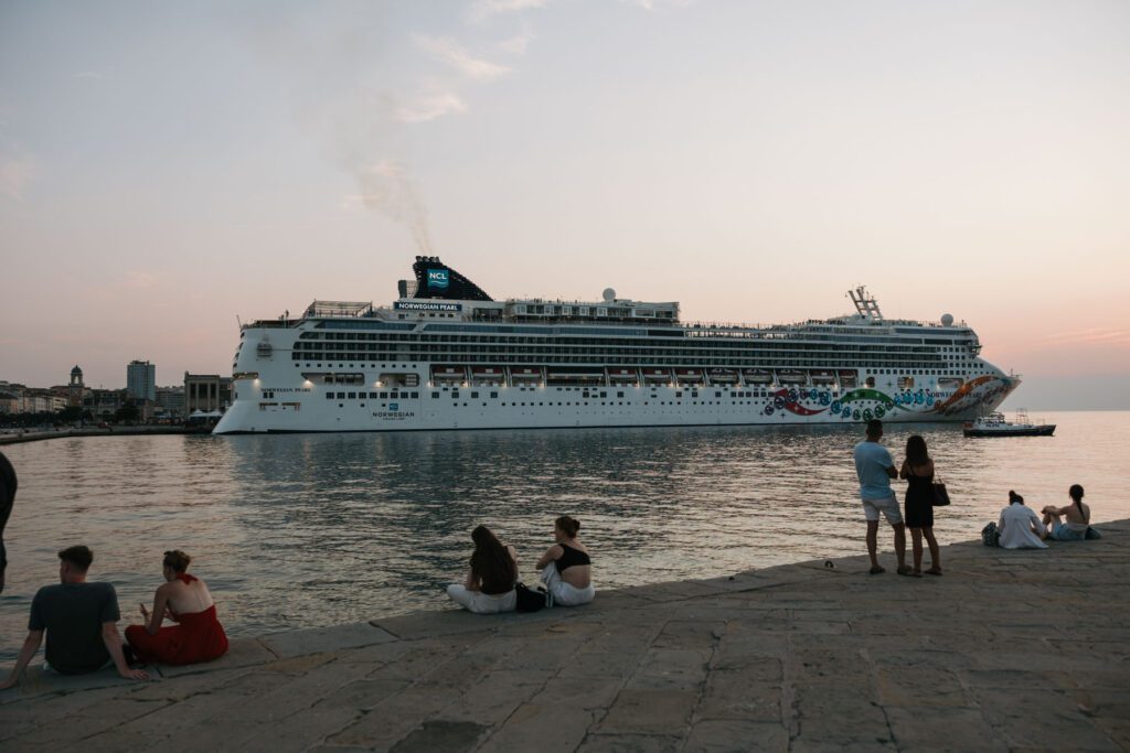 Large cruise ship passing the waterfront in Trieste, Italy as couples sit by the sea during a warm sunset evening