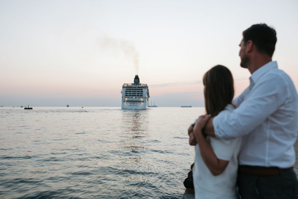 Couple embracing by the sea in Trieste, Italy watching a cruise ship at sunset with calm water and soft evening light