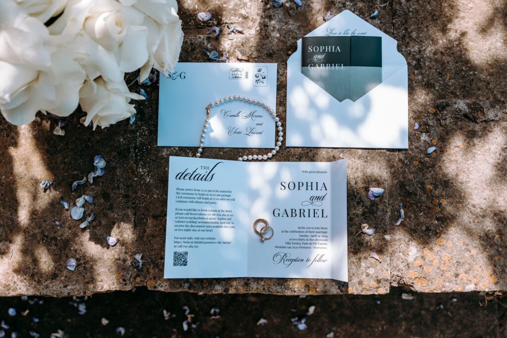 romantic wedding details flat lay with invitation suite and rings under soft natural light surrounded by wisteria petals