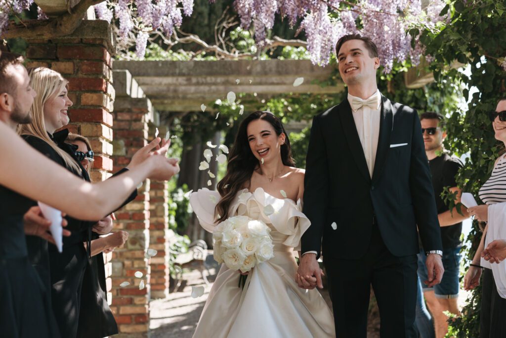 just married couple walking under wisteria with flower petals in Italy