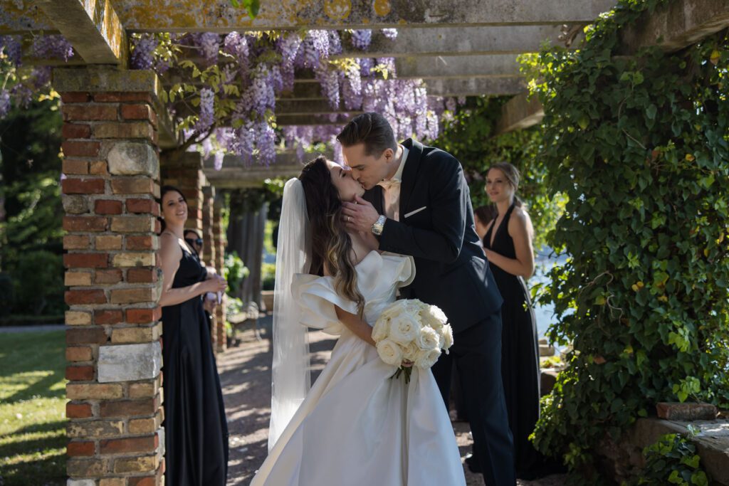 bride and groom kissing under wisteria pergola during destination wedding in Italy