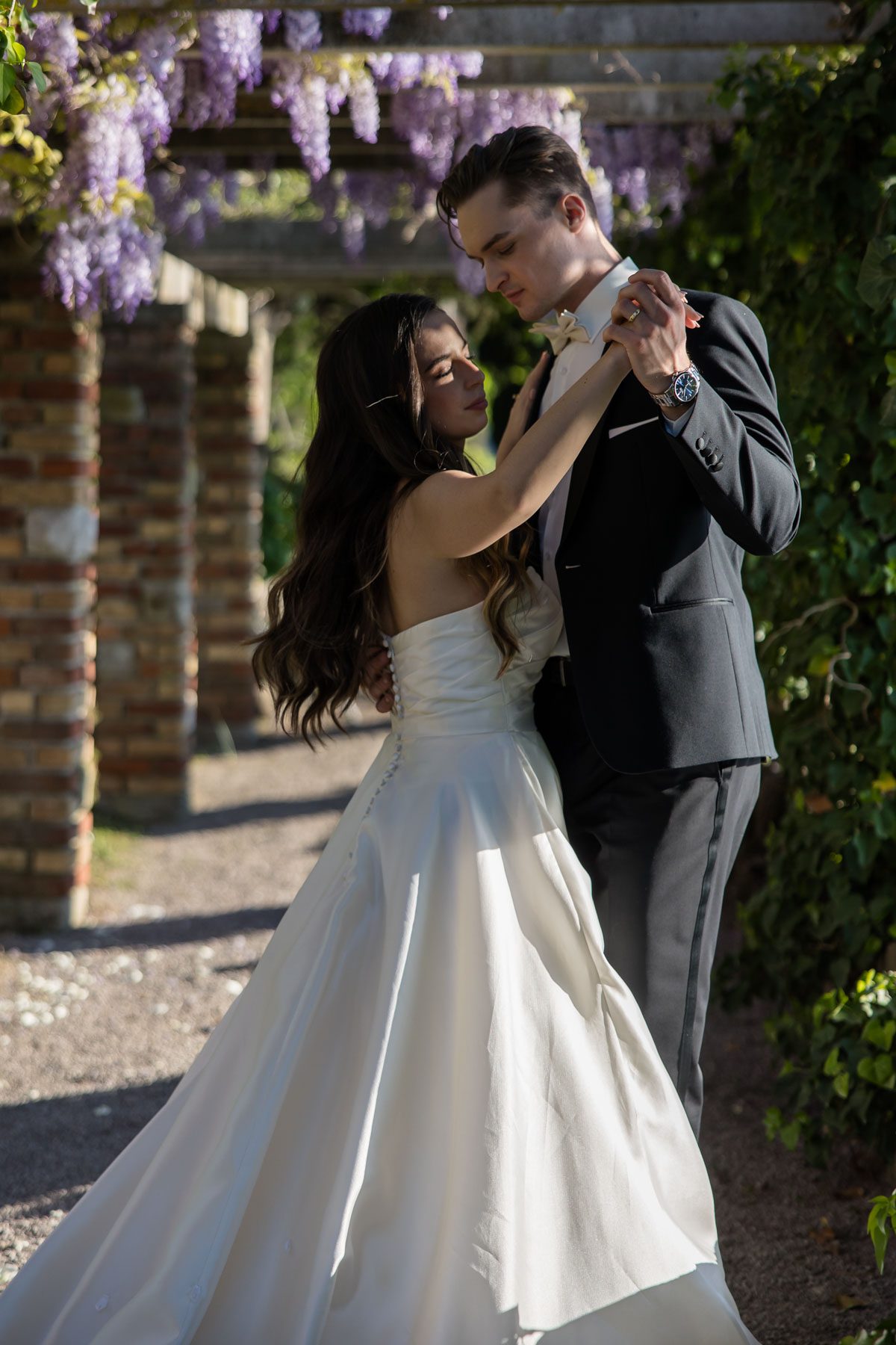 Bride and groom dancing beneath blooming wisteria at Villa Tartini in Strunjan, Slovenia during an elegant destination wedding.