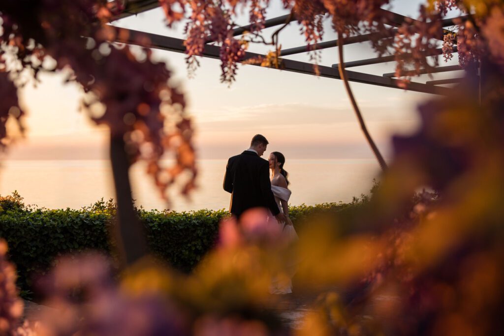 bride and groom at sunset under wisteria overlooking the sea in Italy