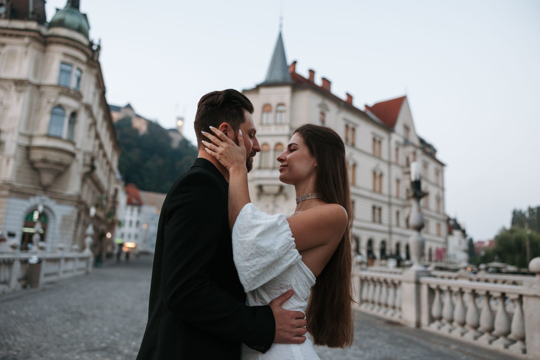 romantic engagement photos Ljubljana Triple Bridge couple with Ljubljana Castle at sunrise