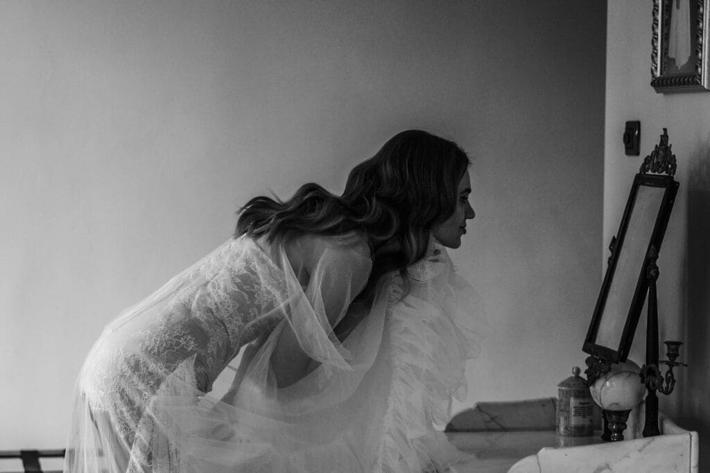 Bride adjusting her dress in front of a mirror, intimate wedding morning moment in soft natural light in an Italian villa