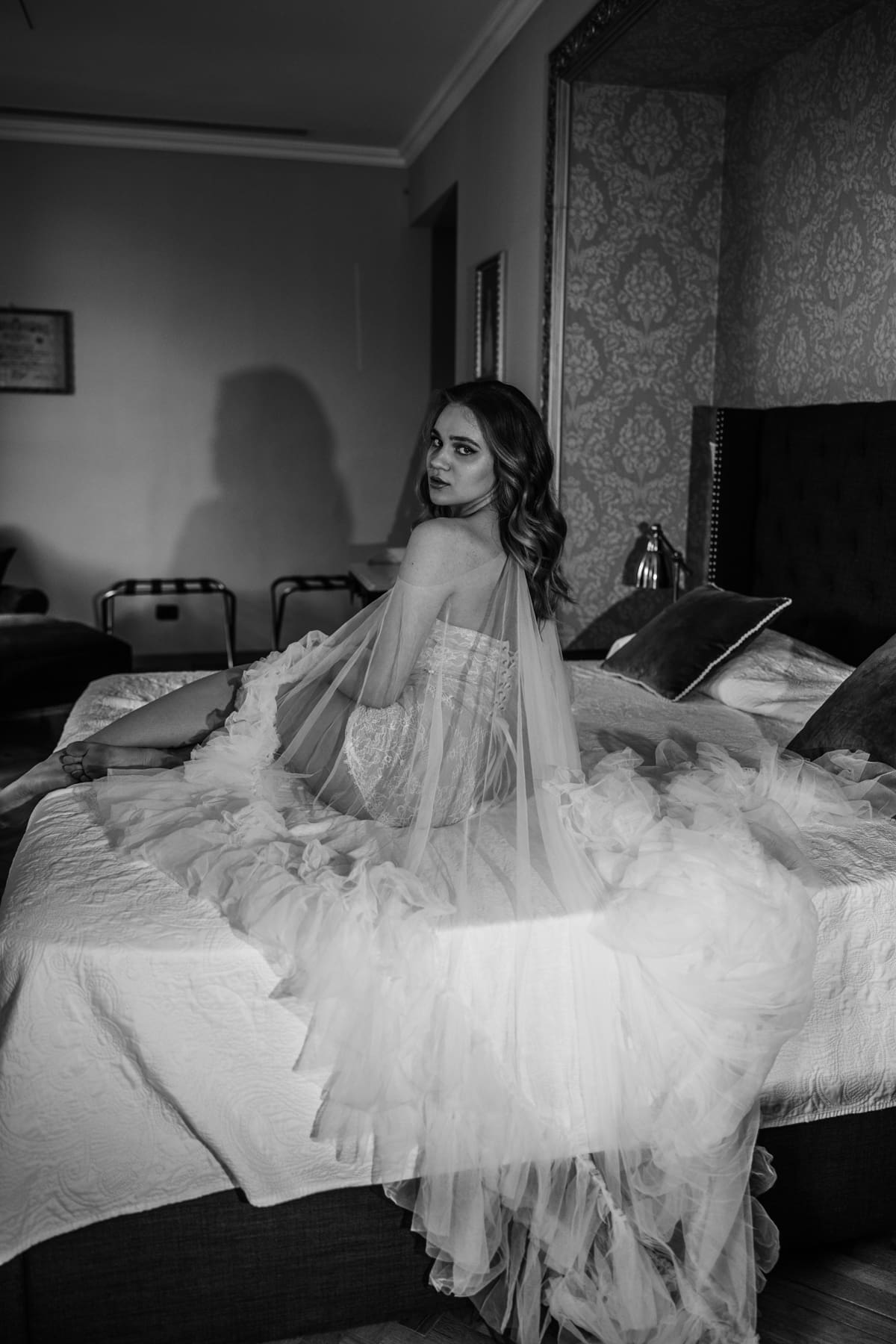 Bride sitting on a bed with long veil, elegant and intimate portrait during wedding morning preparation in Italy