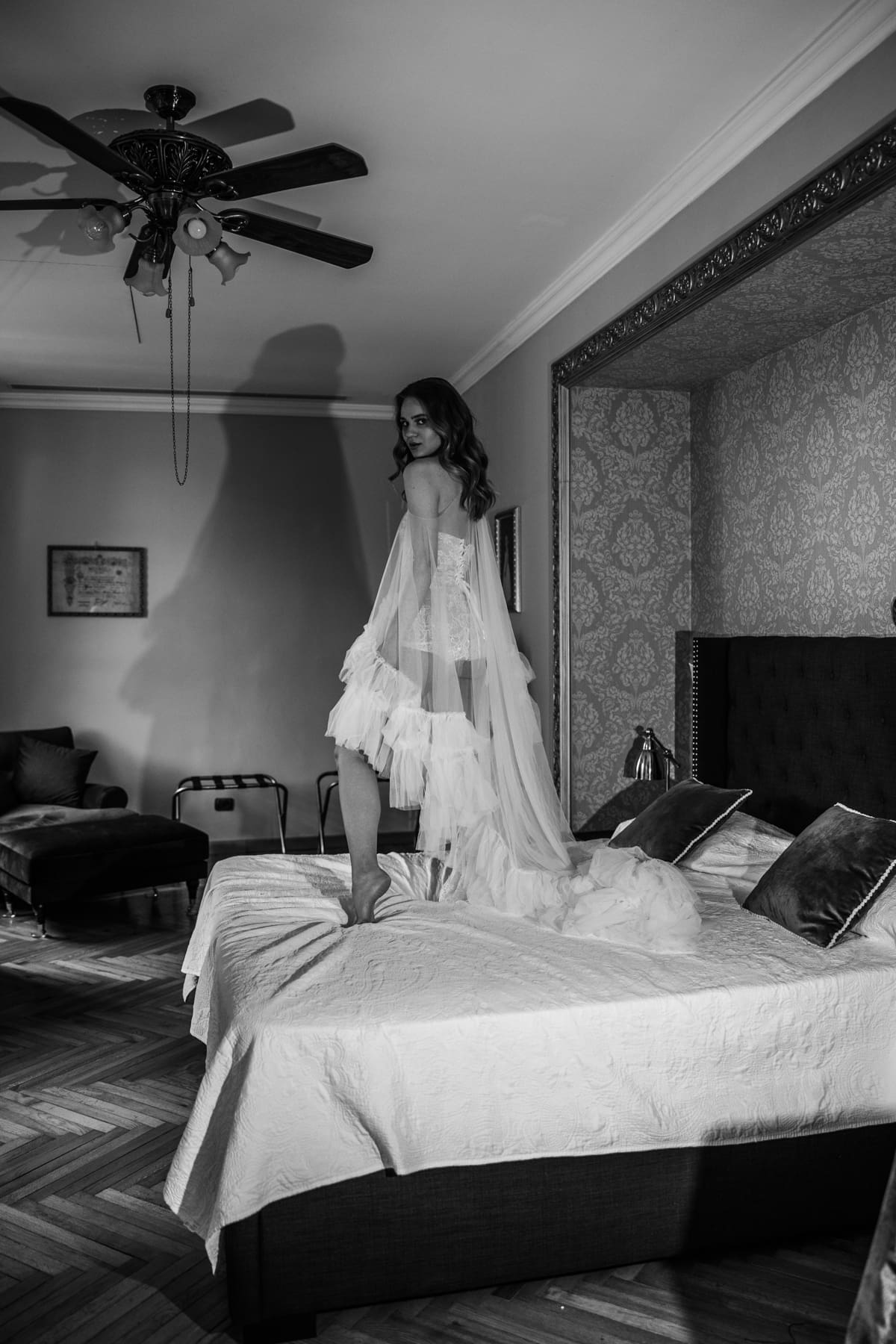 Bride smiling while standing on a bed, relaxed and joyful wedding morning moment in a classic Italian interior