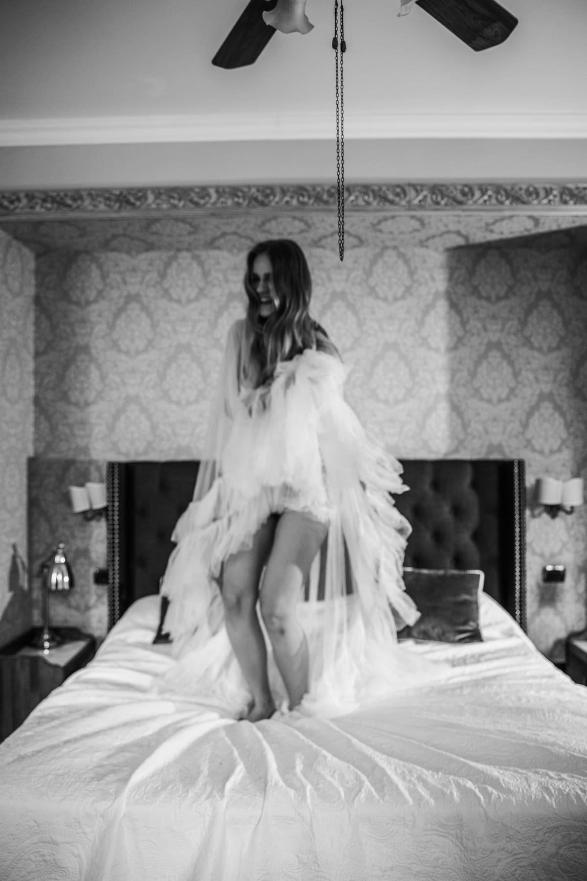 Bride smiling while jumping on a bed, relaxed and joyful wedding morning moment in a classic Italian interior