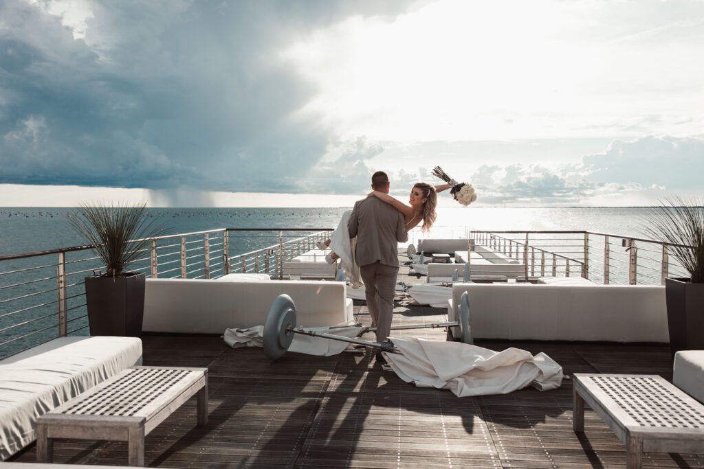 Luxury wedding moment at Portopiccolo in Italy with a groom carrying the bride on a seaside terrace with dramatic ocean views