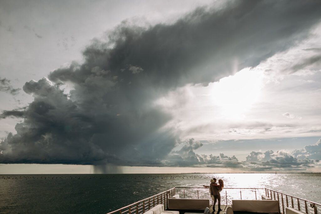 Dramatic seaside wedding moment in Portopiccolo, Italy with a couple overlooking the ocean under a stormy sky and sunlight breaking through clouds