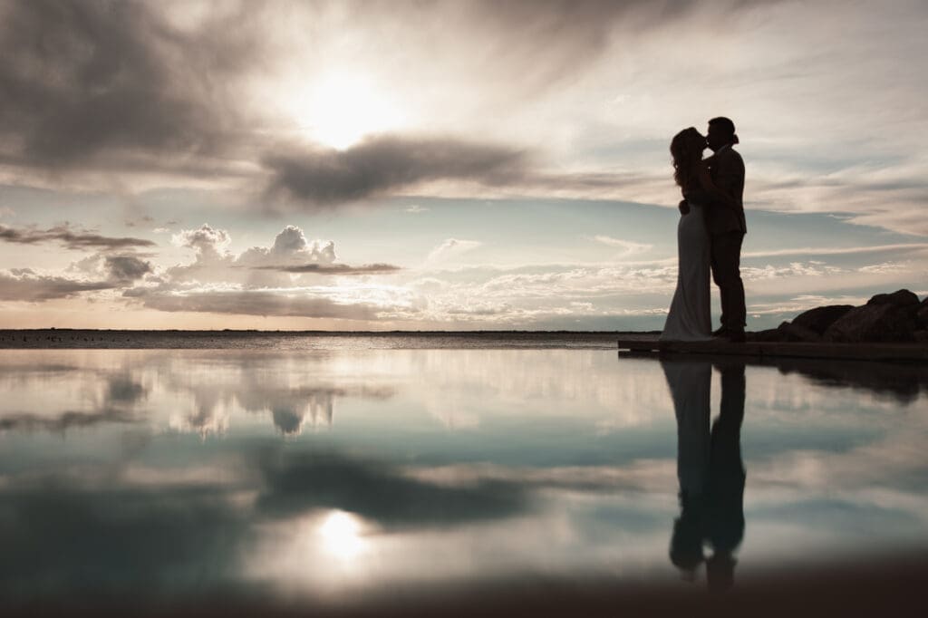 Romantic destination wedding couple silhouette reflected in water near the Adriatic coast close to Trieste, Italy at sunset.