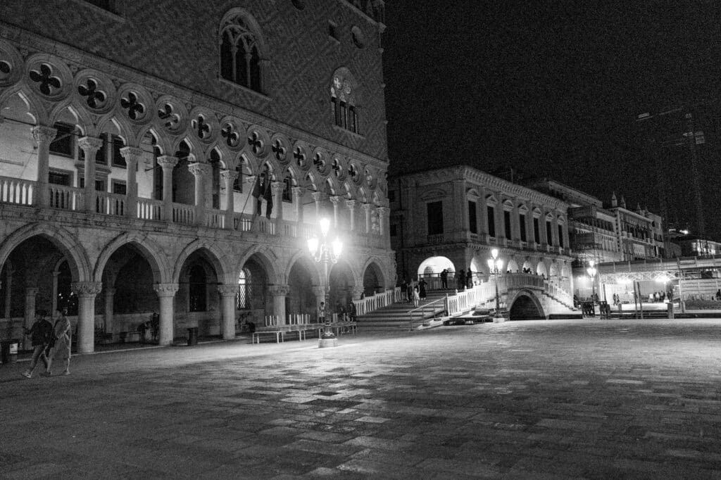 Quiet Piazza San Marco at night with Doge’s Palace and historic Venetian architecture illuminated by street lamps, cinematic black and white Venice photography.