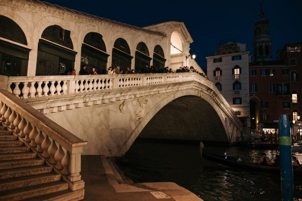 Historic Rialto Bridge illuminated at night over the Grand Canal in Venice, romantic blue hour atmosphere and iconic Venetian architecture in Italy.