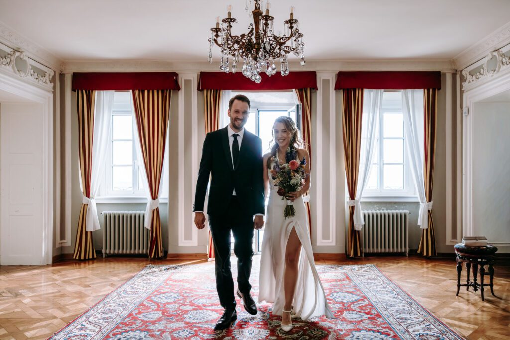 Bride and groom walking inside Villa Bonomo in Trieste Italy elegant wedding interior with chandelier and classic decor