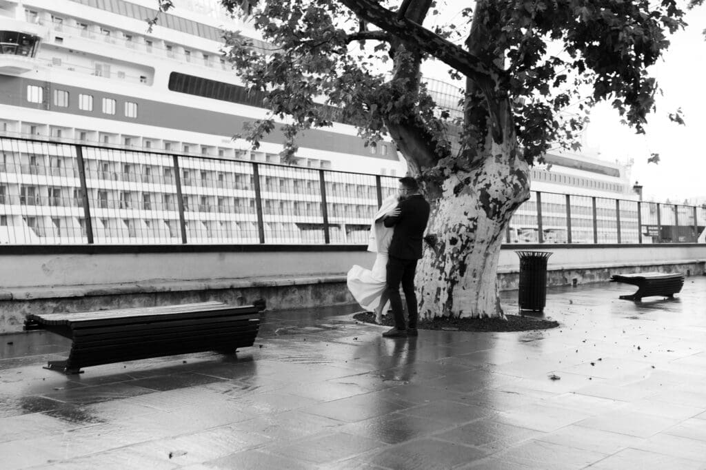 Newlyweds embracing beneath a tree during their first look in Koper, Slovenia with rain-soaked streets and Adriatic views.