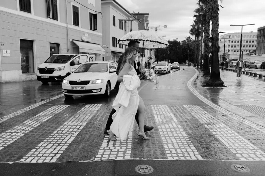 Bride crossing a pedestrian crossing in modern Koper, Slovenia, on a rainy wedding day while walking to her civil wedding ceremony.