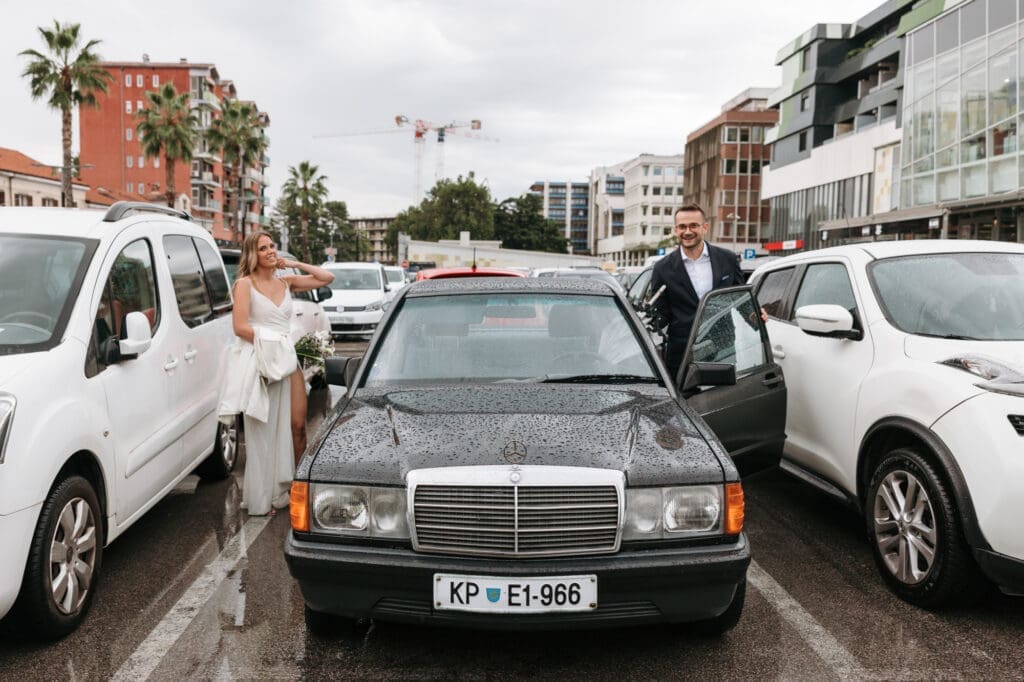 Bride and groom arriving at their vintage Mercedes in Koper, Slovenia, with palm-lined streets and rain-soaked roads on their wedding day.