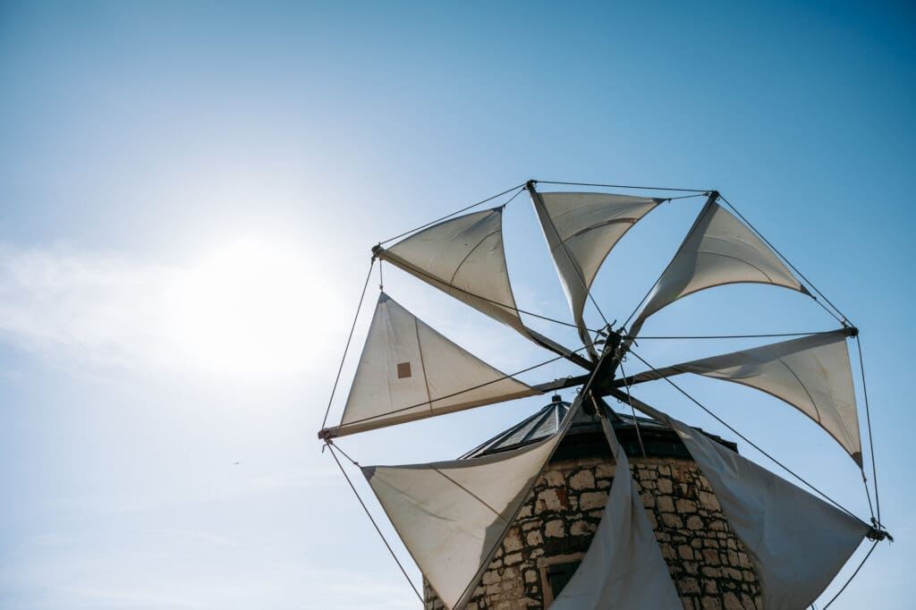 Traditional stone windmill with white sails against a clear blue sky on the Croatian coast during a summer wedding weekend.