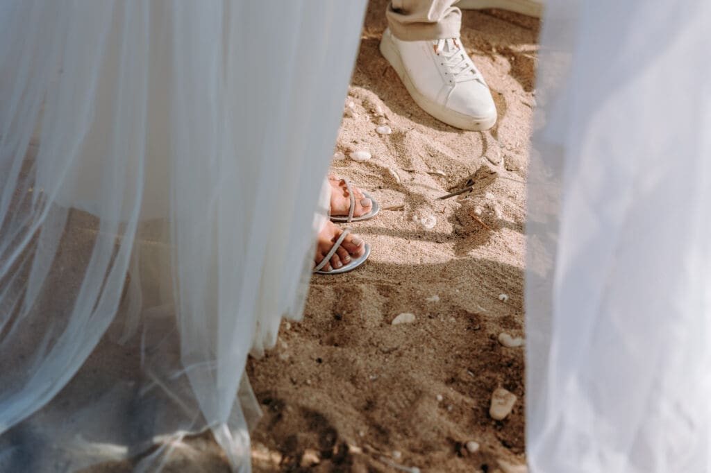 Close-up of the bride and groom standing barefoot in the sand during their beach wedding ceremony on Levan Island in Croatia.