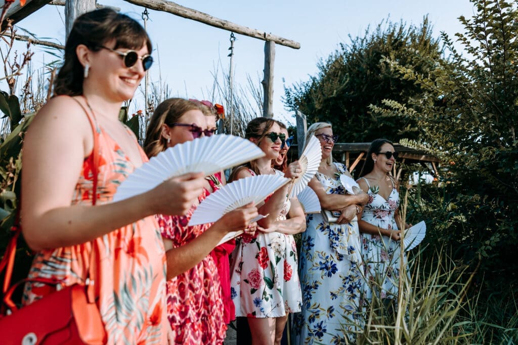 Wedding guests holding white fans while watching a beach wedding ceremony on Levan Island in Croatia during a warm summer afternoon.