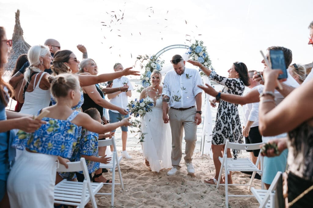 Bride and groom walking through guests throwing olive leaves after their beach wedding ceremony on Levan Island in Croatia.