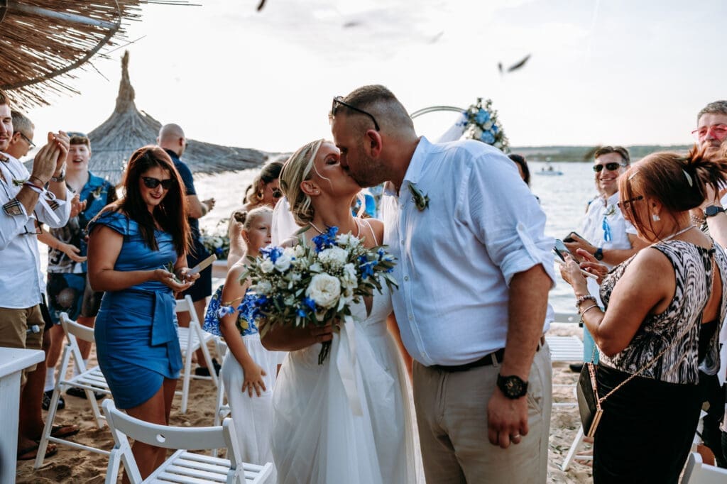 Bride and groom kissing after their intimate beach wedding ceremony on Levan Island in Croatia surrounded by family and friends by the sea.