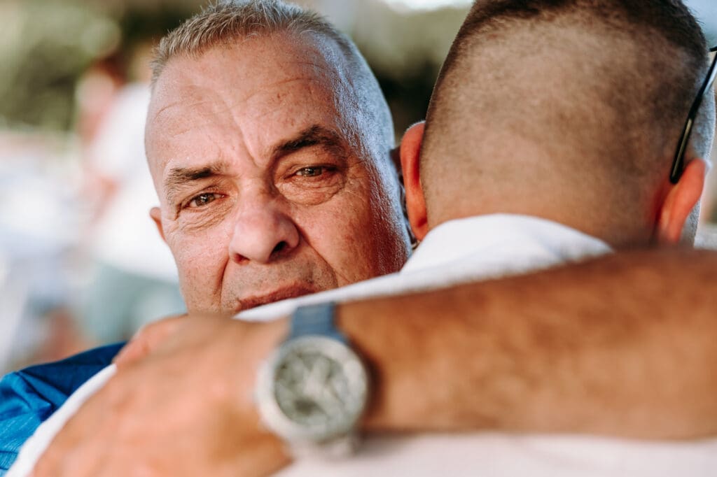 Emotional close-up moment of a father hugging his son before a beach wedding ceremony on Levan Island in Croatia.