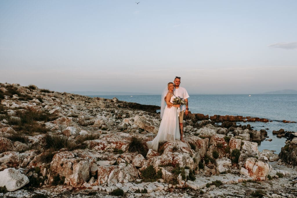 Bride and groom posing on the rocky coastline of Levan Island in Croatia during sunset after their intimate beach wedding ceremony.
