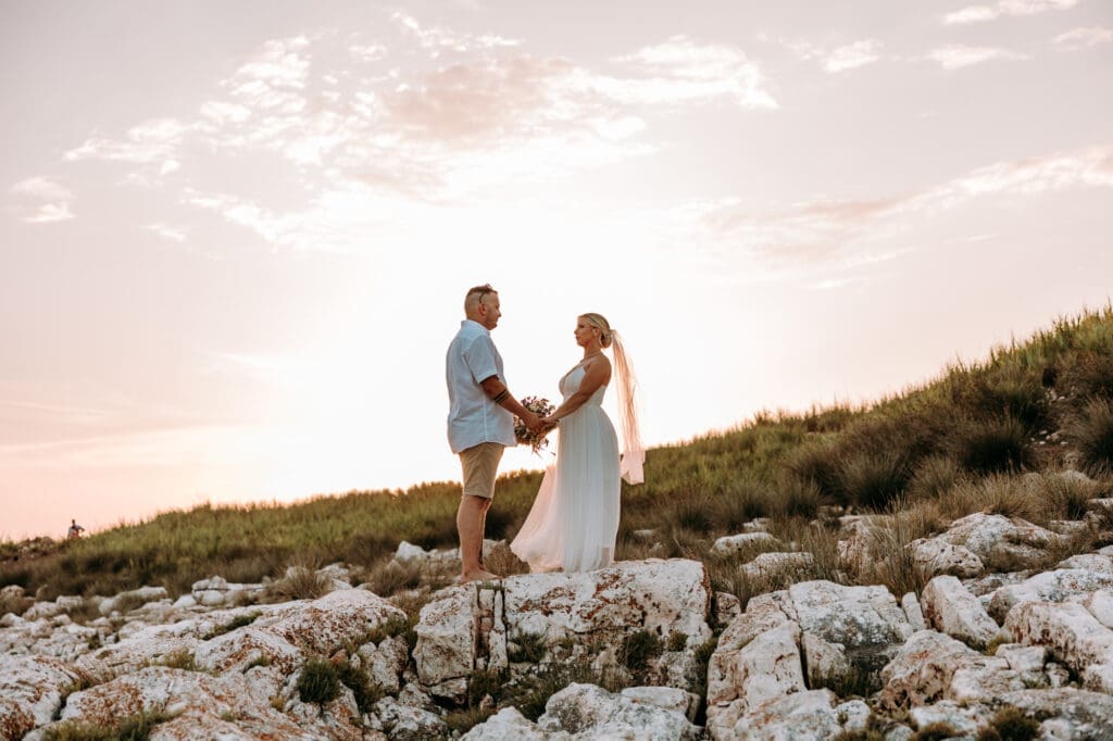 Bride and groom holding hands on the rocky shores of Levan Island in Croatia during a romantic sunset portrait session by the Adriatic Sea.