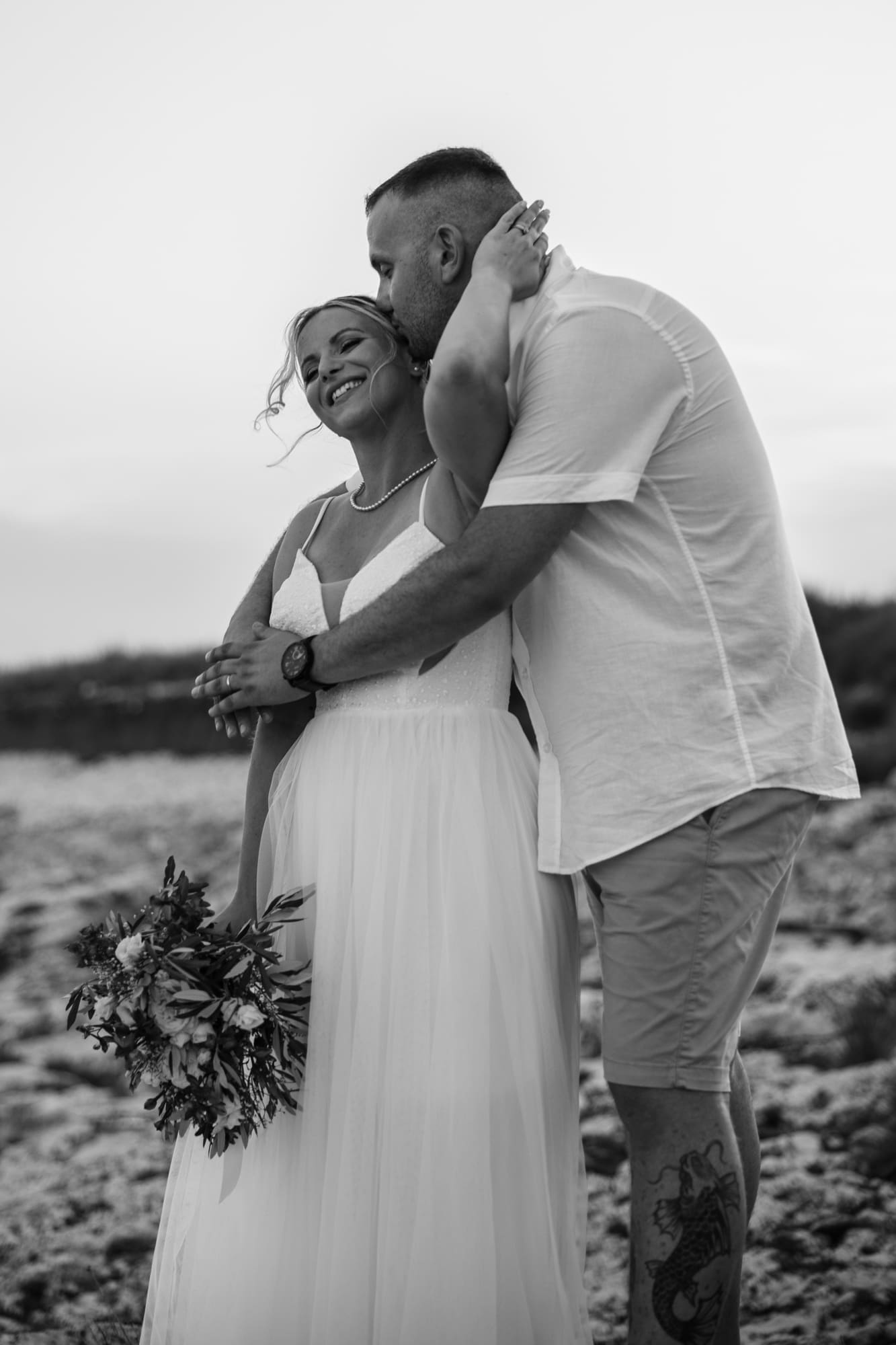 Black and white portrait of the bride and groom embracing on the rocky coastline of Levan Island in Croatia after their intimate beach wedding ceremony.