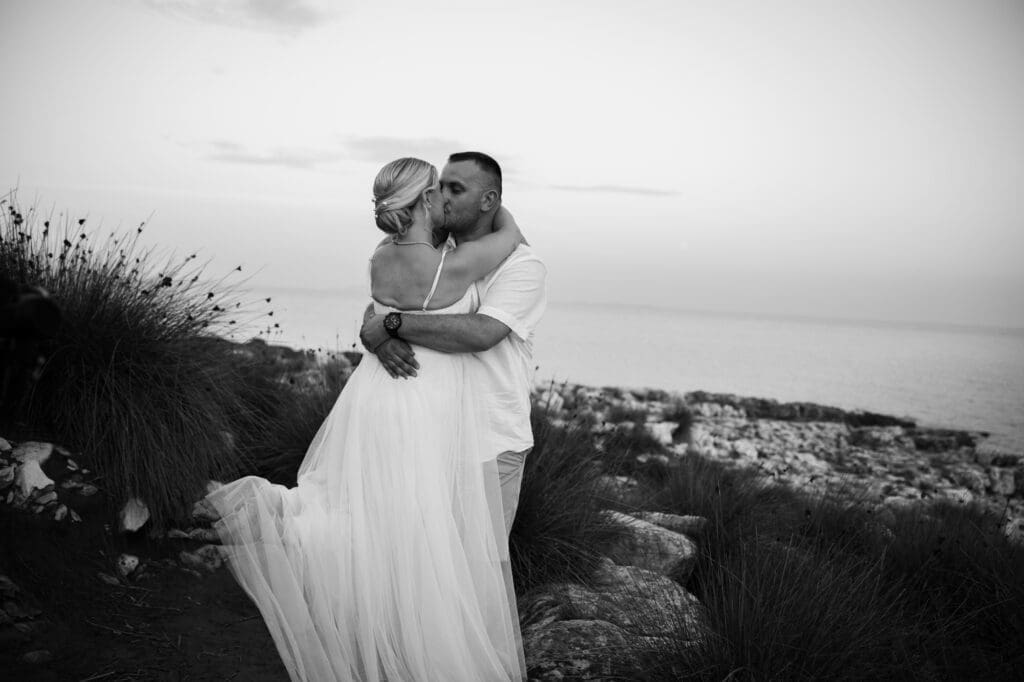 Black and white portrait of the bride and groom embracing on the rocky coastline of Levan Island in Croatia at sunset after their intimate beach wedding ceremony.