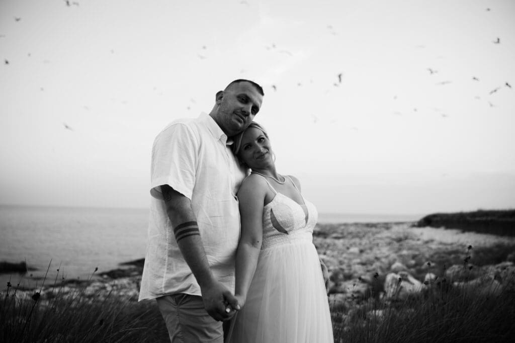 Black and white portrait of the bride and groom holding hands by the Adriatic Sea on Levan Island in Croatia during sunset after their beach wedding.