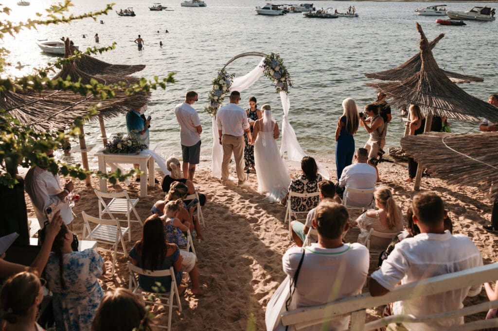 Intimate beach wedding ceremony on Levan Island in Croatia with guests gathered around the couple beside the Adriatic Sea during golden hour.