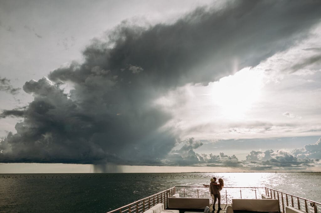 Zala and Matej standing together in Portopiccolo with dramatic storm clouds over the Adriatic coast.