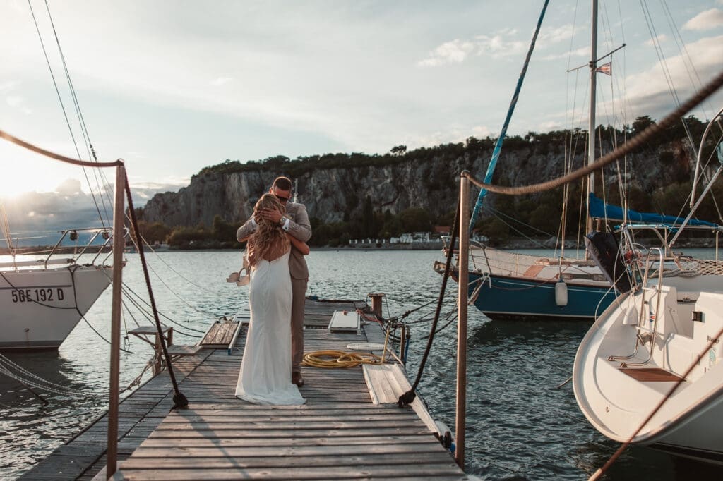 Zala and Matej embracing on the marina dock during sunset wedding portraits in Sistiana, Italy.
