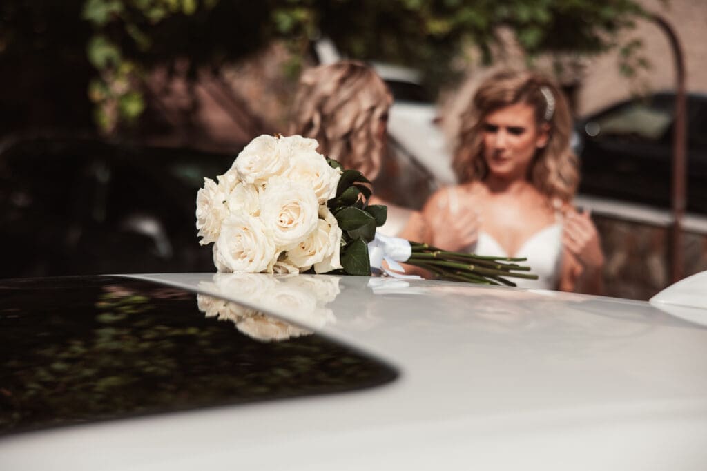 White bridal bouquet resting on the wedding car with Zala getting ready before the ceremony in Šmihelj.