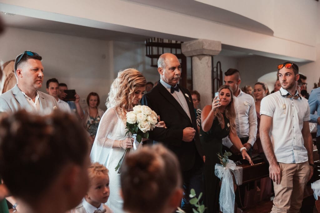 Zala walking with her father through the Church of St. Michael during the wedding ceremony in Šmihelj, Slovenia.
