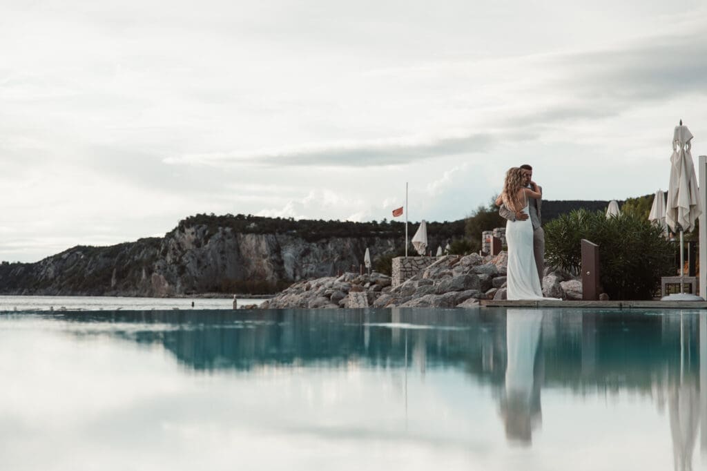 Zala and Matej embracing beside the infinity pool during romantic wedding portraits in Portopiccolo, Italy.