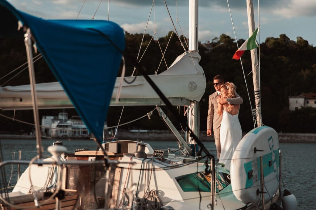 Zala and Matej standing together on Matej's sailboat during wedding portraits in Sistiana, Italy.
