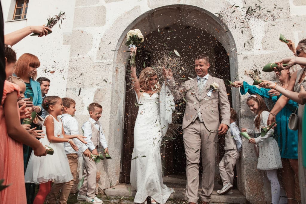 Zala and Matej celebrating outside the Church of St. Michael in Šmihelj as guests throw flower petals after the ceremony.