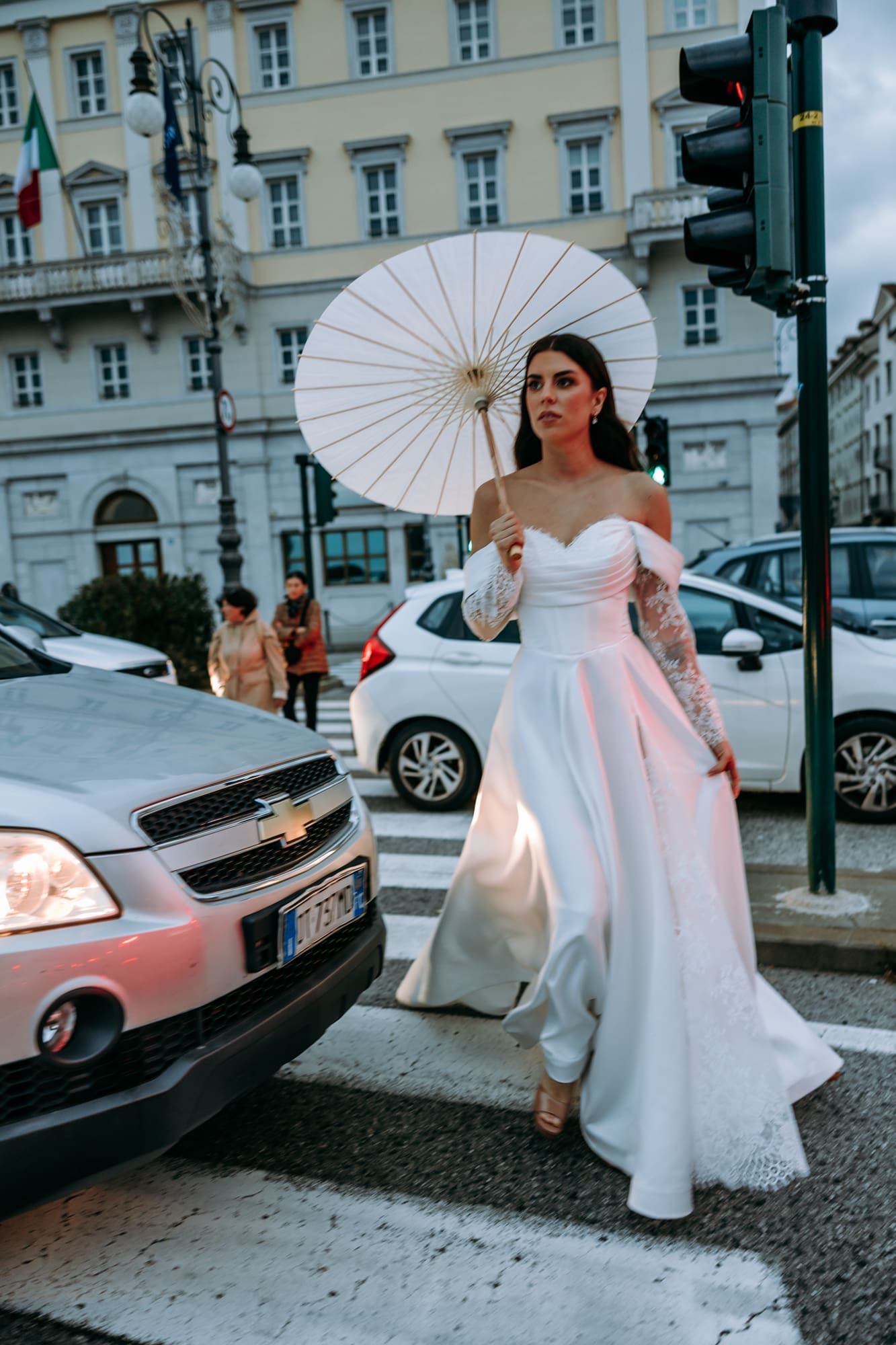 Bride walking through the streets of Trieste with a white parasol during an urban wedding photoshoot in the historic city center, ItalyD