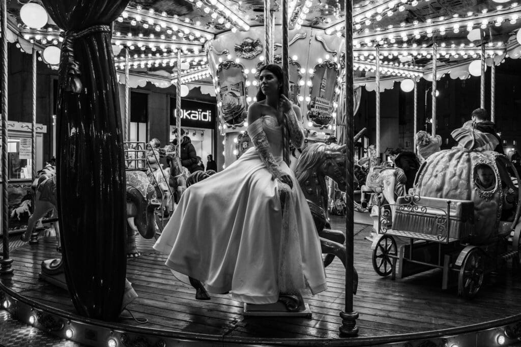 Bride riding a vintage carousel in Piazza della Borsa during a black and white editorial wedding photoshoot in Trieste, Italy