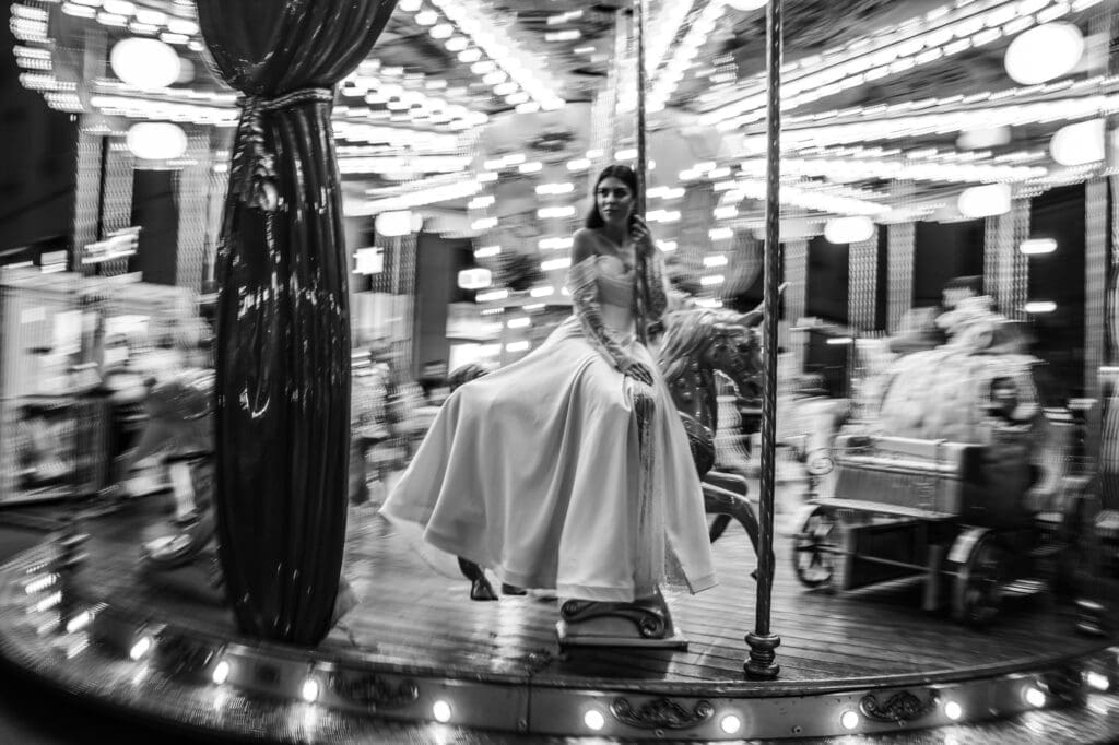 Bride riding a vintage carousel in Piazza della Borsa during a black and white editorial wedding photoshoot in Trieste, Italy