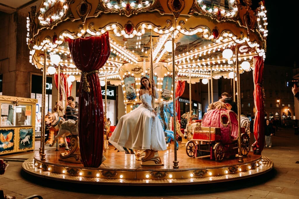 Bride sitting on a vintage carousel during a romantic nighttime wedding photoshoot in Trieste, Italy