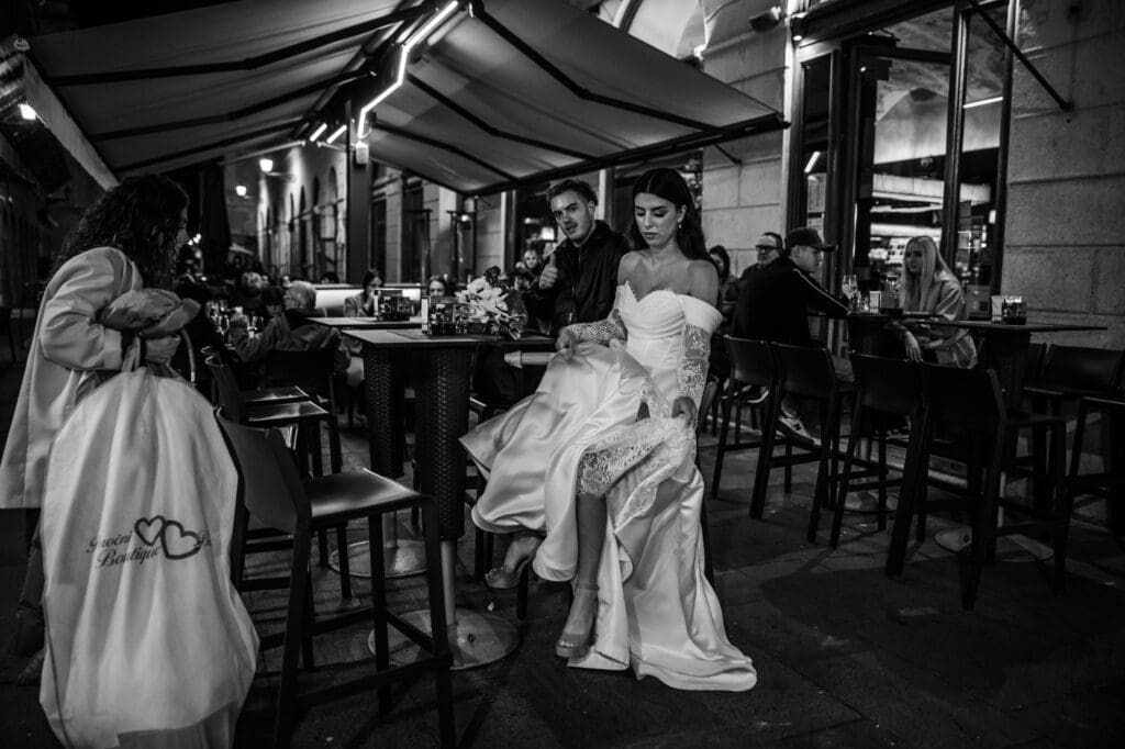 Bride stopping for an Aperol Spritz at Urbanis in Piazza della Borsa during a nighttime wedding photoshoot in Trieste, Italy