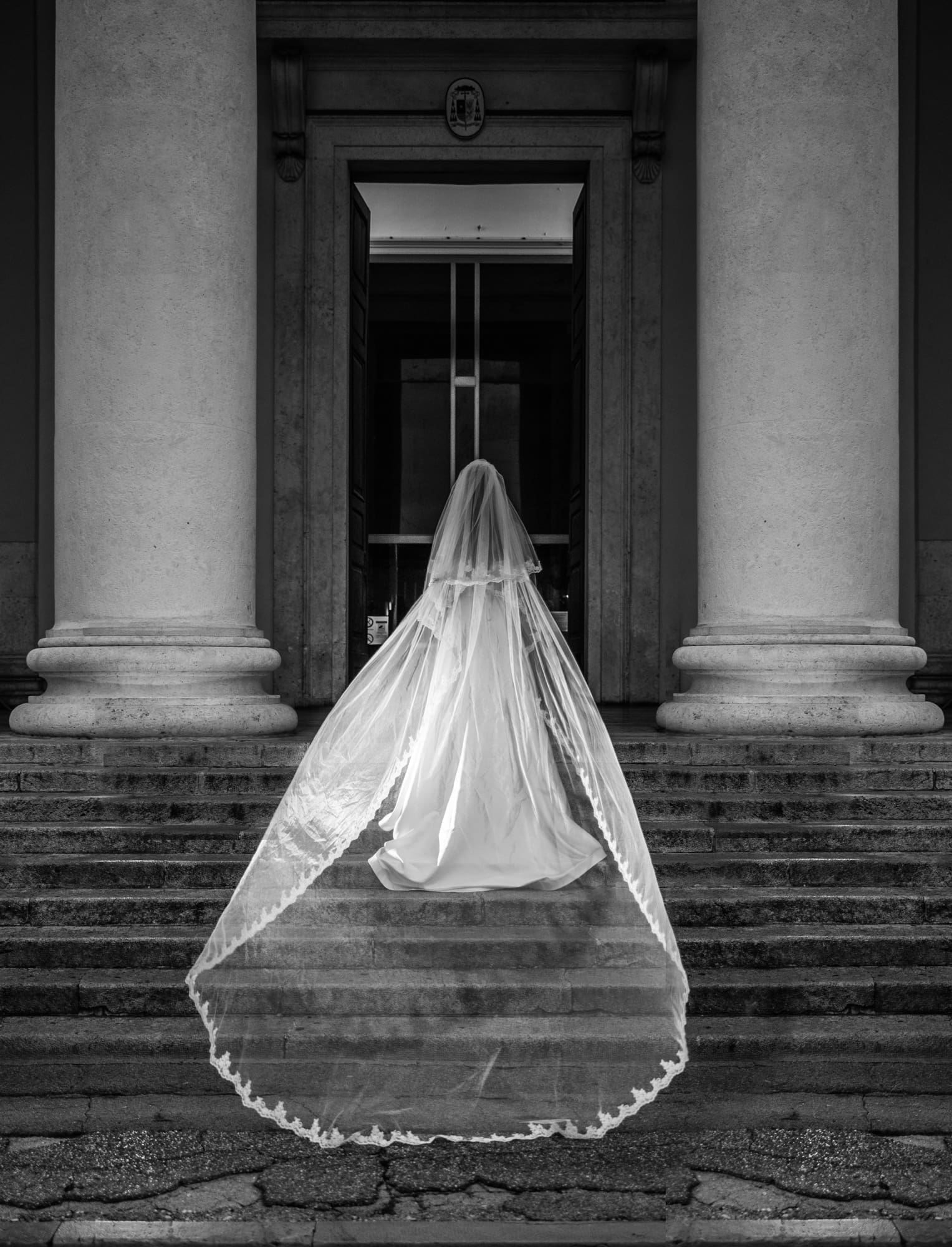 Bride with a cathedral-length veil standing on the steps of Sant’Antonio Nuovo during a black and white wedding photoshoot in Trieste, Italy