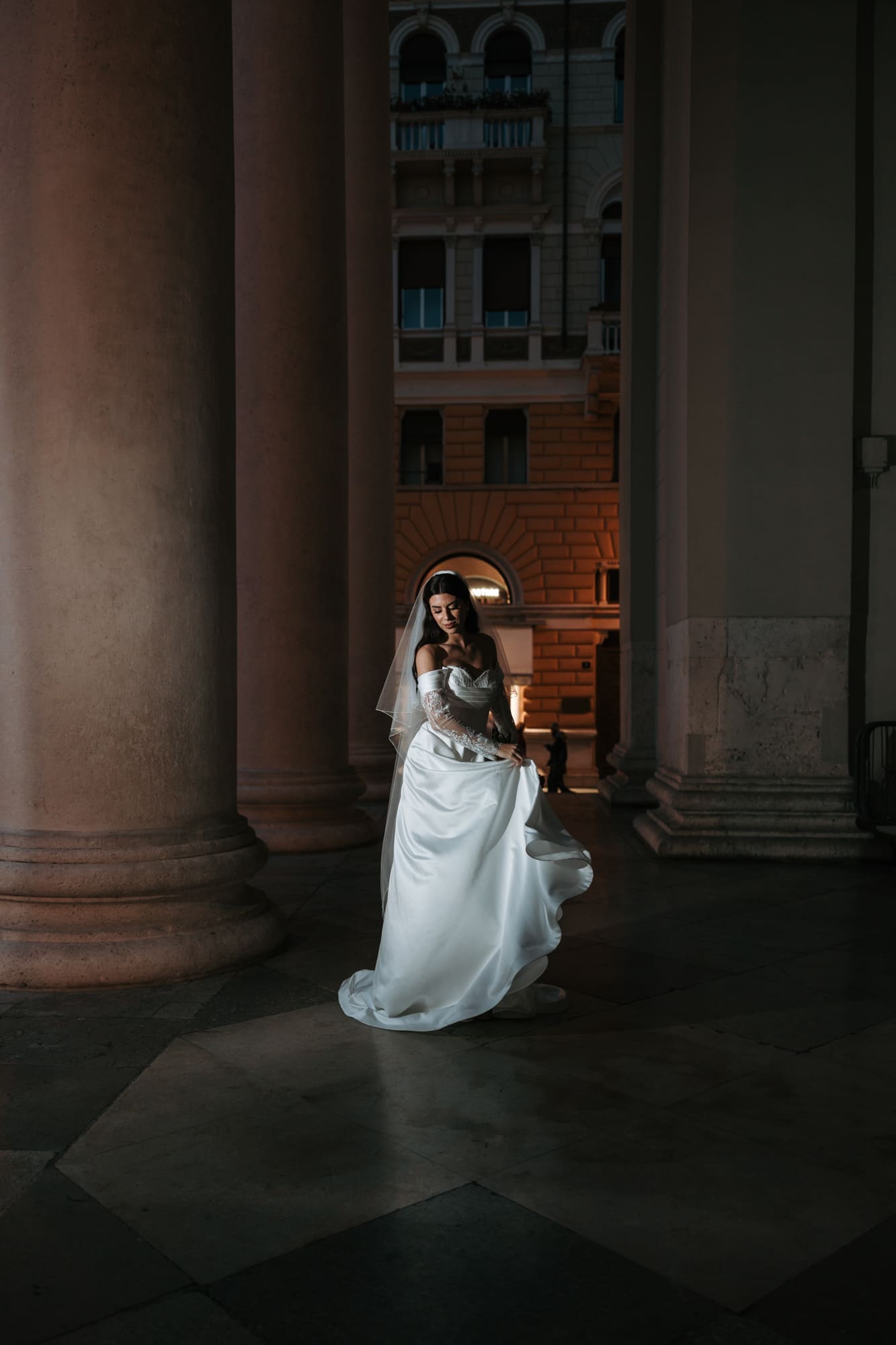 Bride standing between the grand columns of Sant’Antonio Nuovo during an evening wedding photoshoot in the historic center of Trieste, Italy
