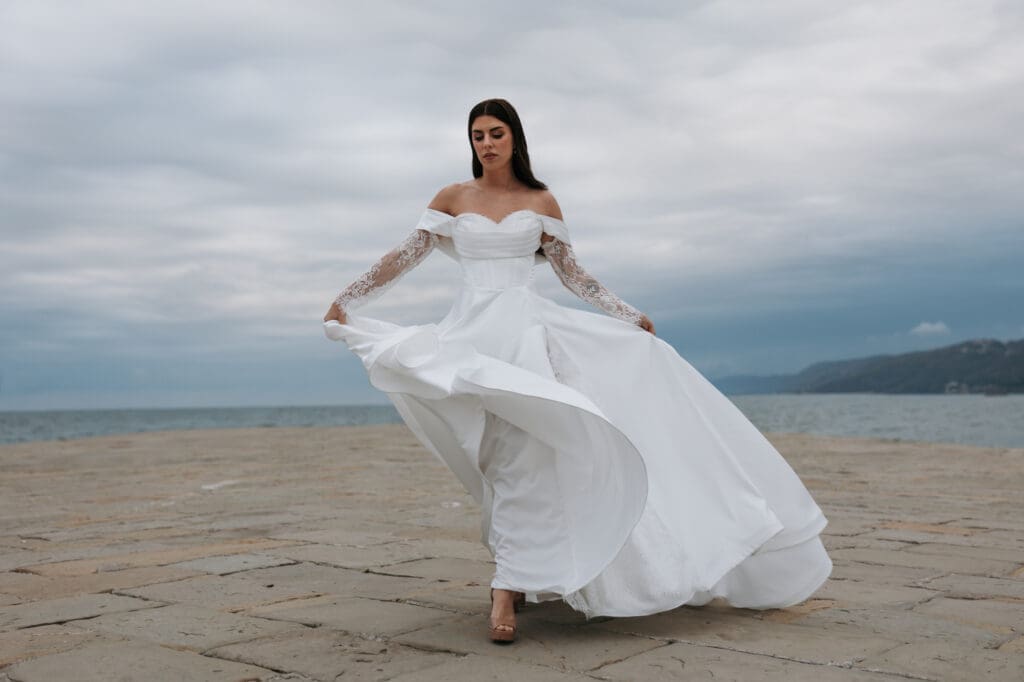 Bride in a flowing wedding dress walking along the waterfront during a romantic photoshoot in Trieste, Italy