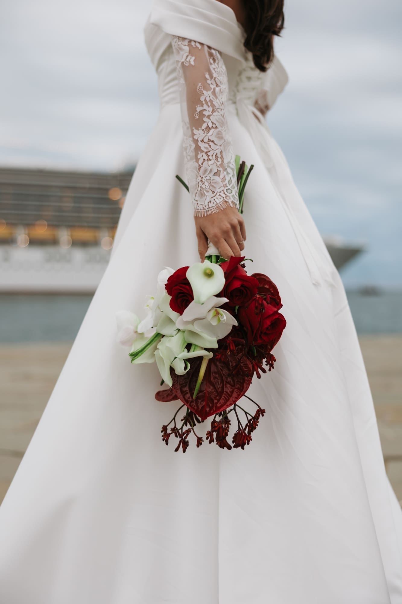 Close-up of a bride holding an elegant bouquet of white calla lilies and red roses during a wedding photoshoot at Molo Audace in Trieste, Italy